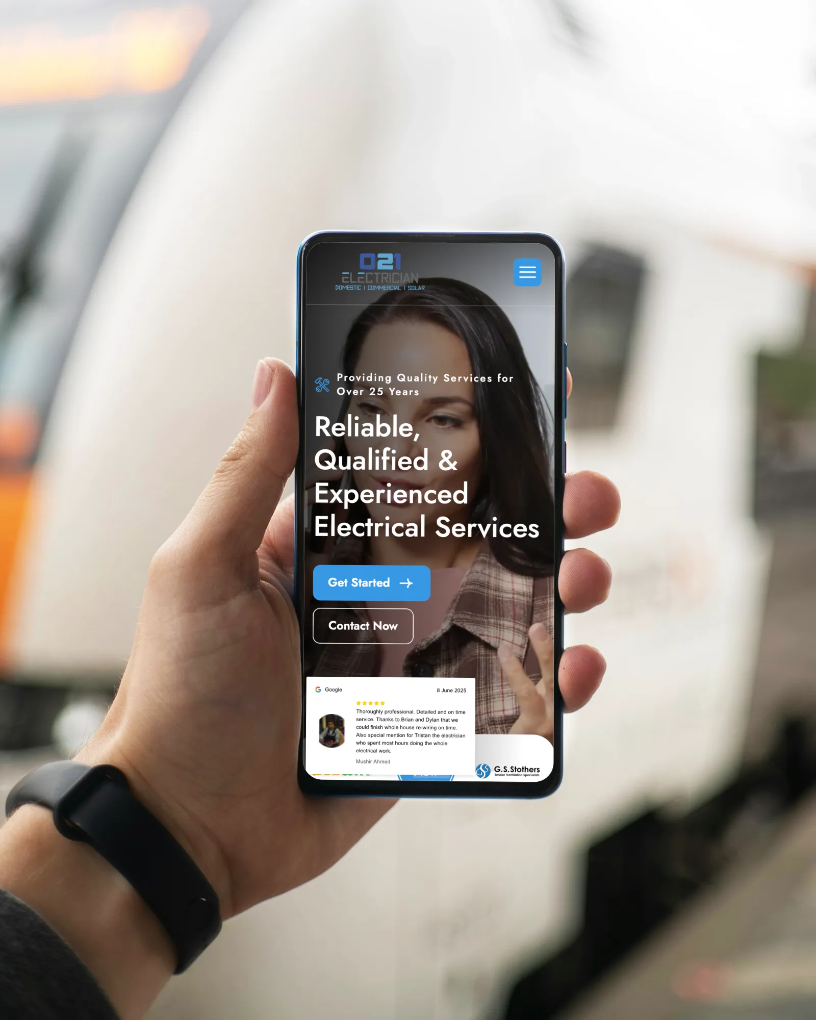 A hand holding a smartphone displaying the 021 Electrician website, showing “Reliable, Qualified & Experienced Electrical Services.” SEAI Certified badge appears above, with service highlights such as fast emergency support and 24-hour electrician service in Cork shown on the right.