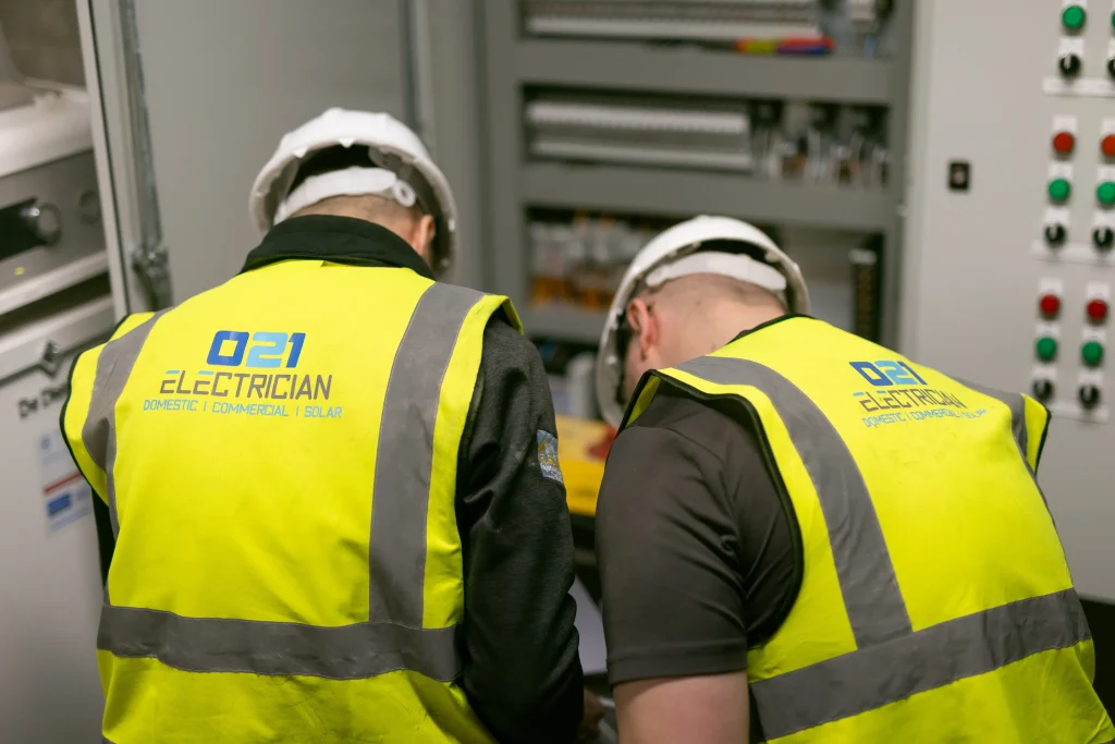 Two 021 Electrician technicians in high-visibility jackets working on an electrical panel in Cork, providing domestic, commercial, and solar electrical services