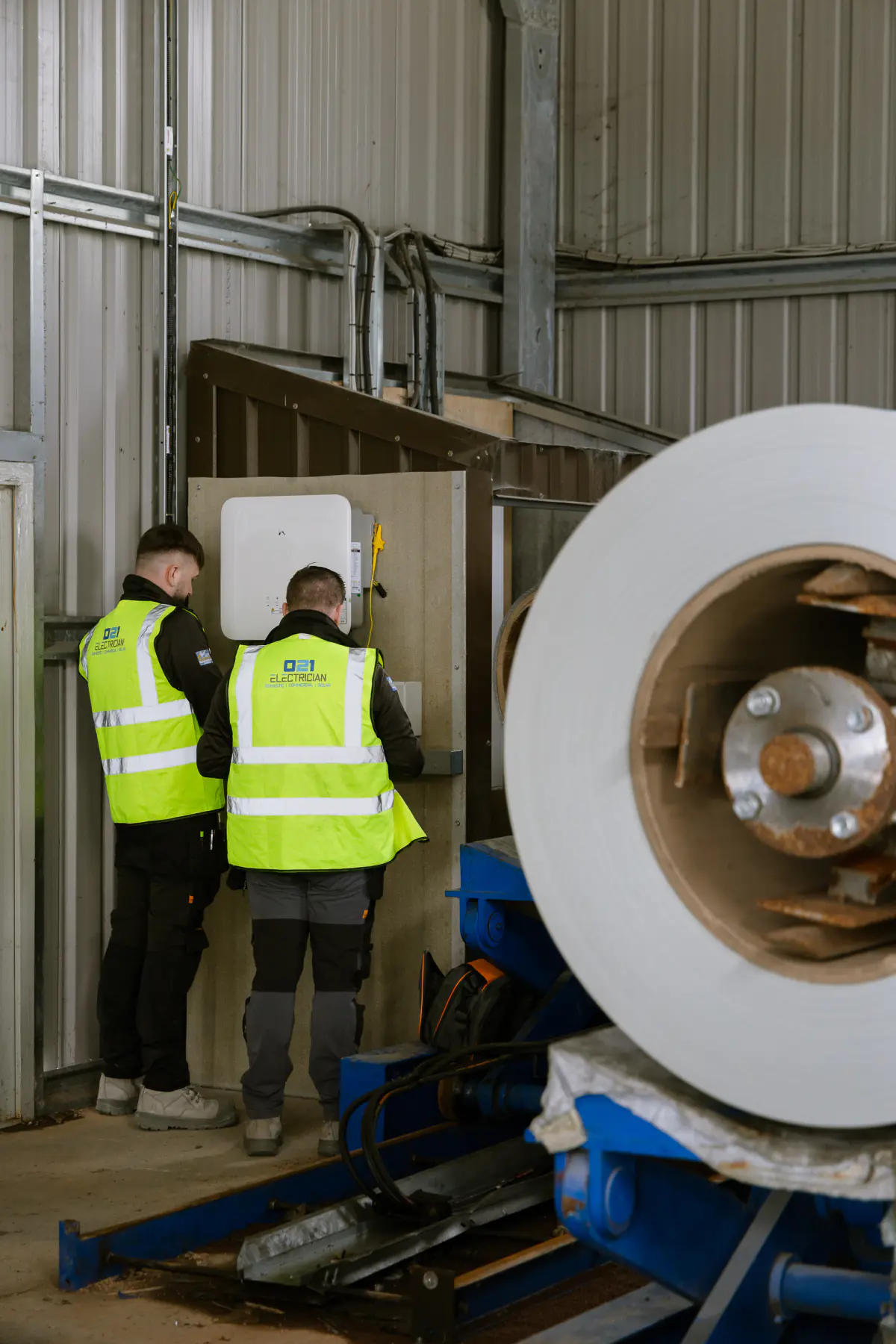 Two 021 Electrician team members working on a commercial solar inverter inside an industrial building.