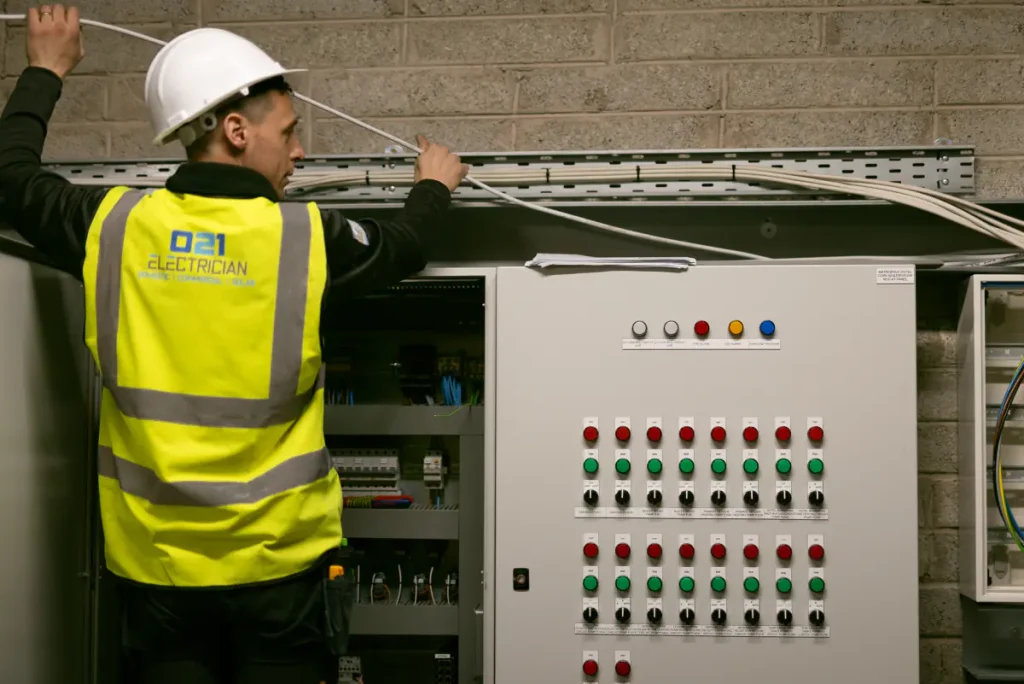 021 Electrician team member installing wiring above a commercial electrical control panel in Cork.